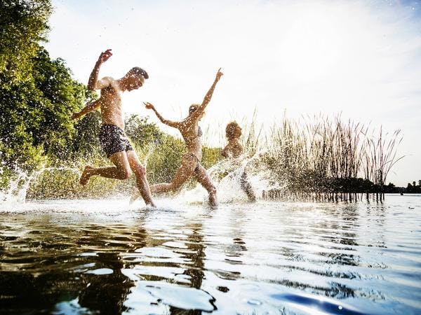 Tre personer løper uti et vann for å bade