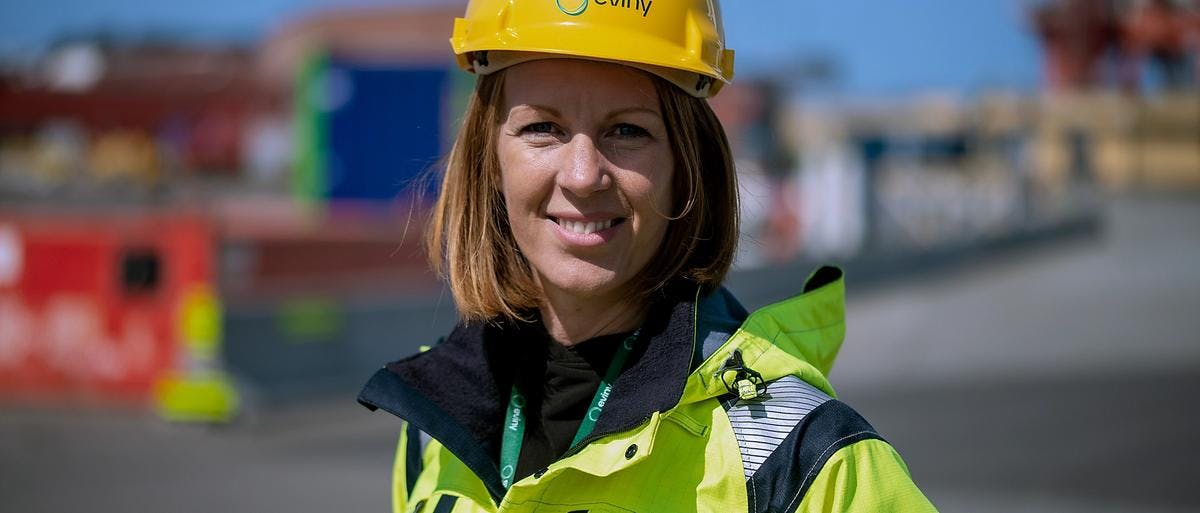 Dame i gul uniform og hjelm på et industriområde